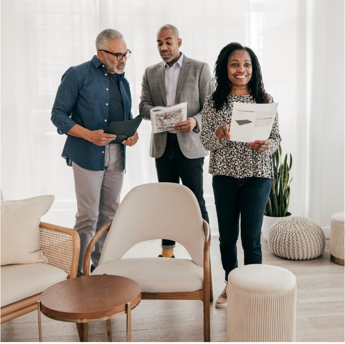 Three people standing in a living room holding paperwork.