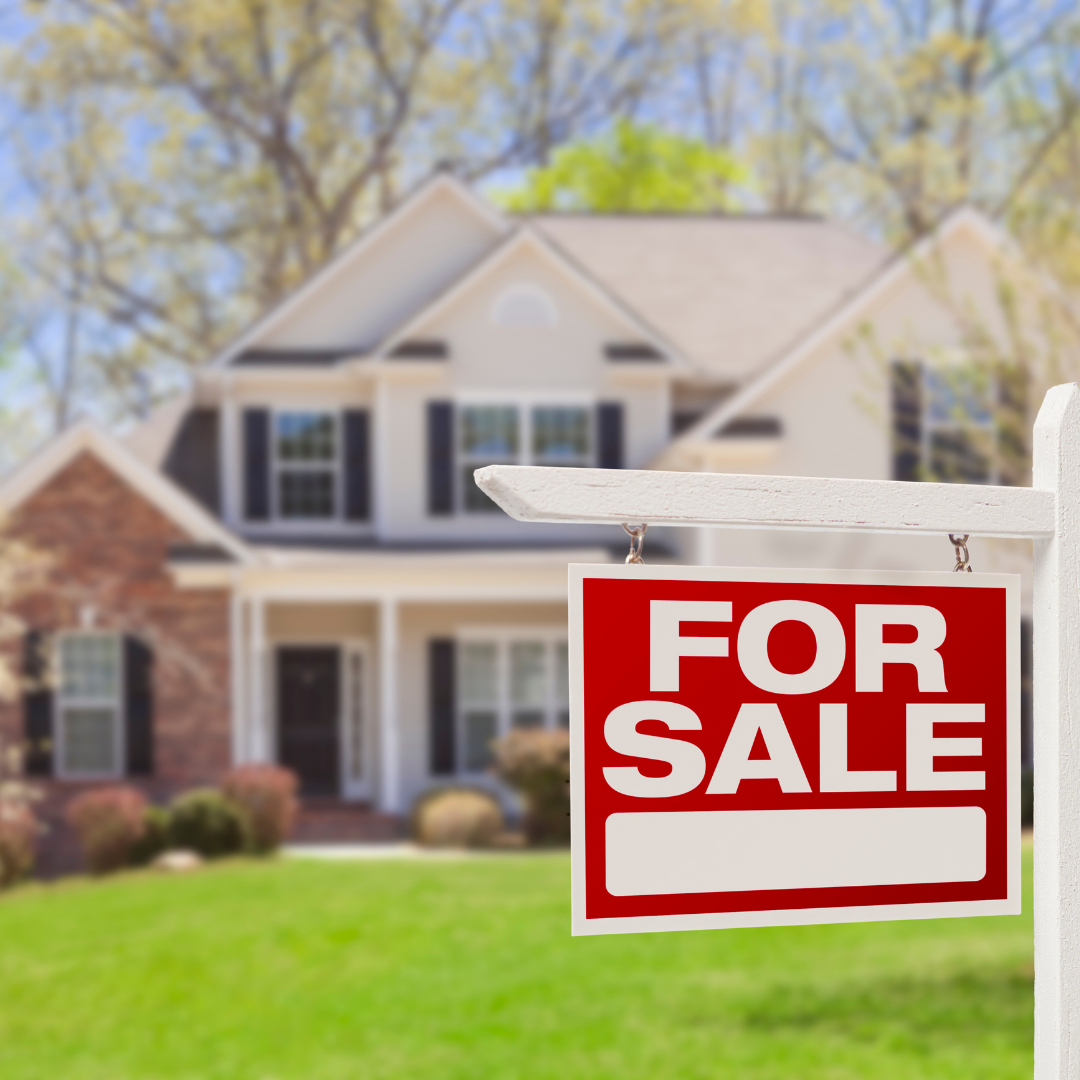 A "For Sale" sign hangs in front of a two-story house with a mix of brick and siding exterior, black shutters, and an inviting front porch. The well-maintained lawn and trees in the background suggest it is a suburban home on a sunny day.