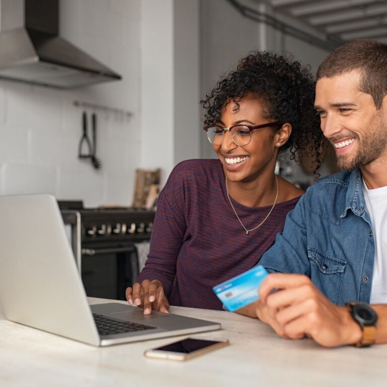 a couple smiling as they look at a laptop while holding a credit card.