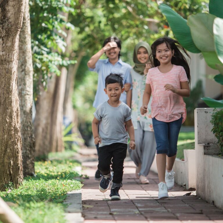 a family of 4- 2 young children and parents walking on a path. The children happily run ahead of the parents.