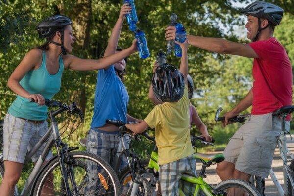 A family of 4 standing over their bicycles as they lift their water bottles in a sign of victory.