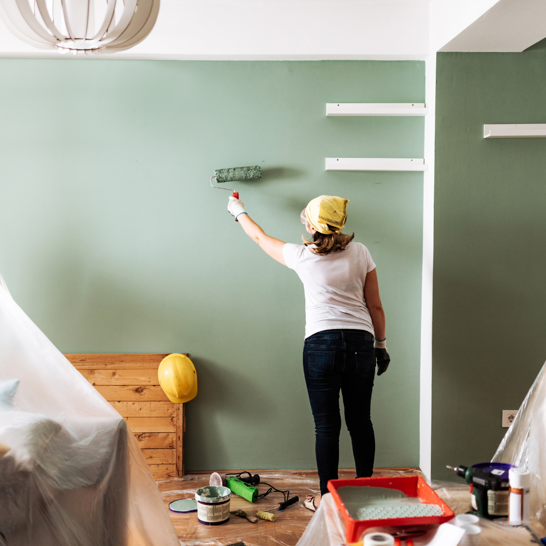 a woman is standing and painting a wall green in color with a roller brush.