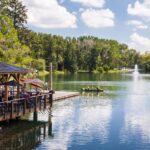 a beautiful park of a lake with small boat and restaurant on the left.