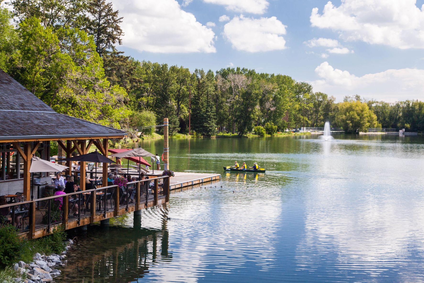 a beautiful park of a lake with small boat and restaurant on the left.
