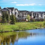 A row of houses with trees by a lake.