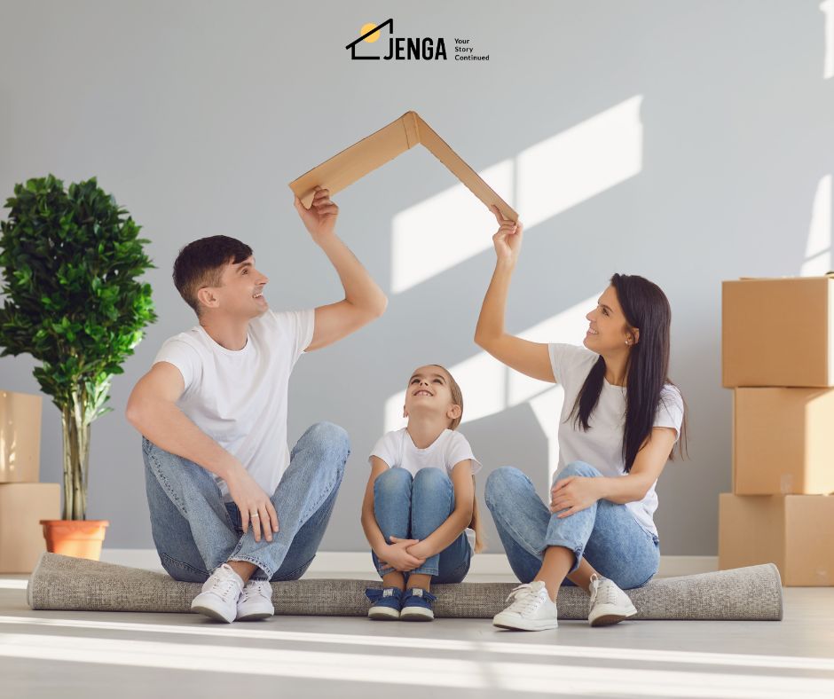 A photo of a couple sitting with a child in in between them as they make a shape of a roof with their hands holding a cardboard.